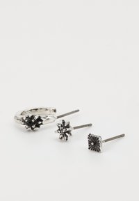 Ensemble de bijoux en ton argent comprenant une boucle d'oreille texturée et deux clous d'oreilles avec des designs floraux et des accents noirs centraux.