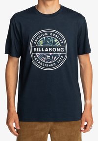 Námořnická modrá bavlněná tričko s kulatým logem Billabong a vícerozbarvenými vlnovými vzory, kulatý výstřih a krátké rukávy.