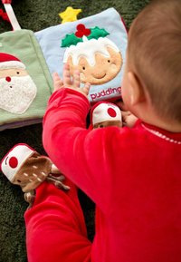 Textiles Aktionsbuch mit weichen, bunten Seiten und gestickten Illustrationen von Santa und Pudding. Ein Kind in roten Pyjamas interagiert mit den Plüsch-Elementen.