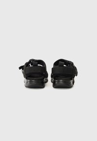 Black sandals with adjustable straps, rubber soles, and a textured fabric upper. The design features an open back and secure fit.