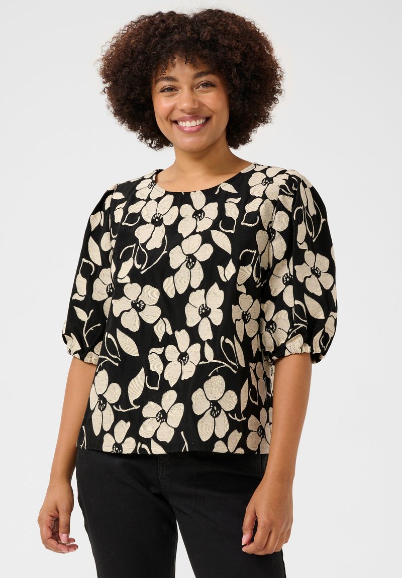 Haut noir avec un motif floral en crème, présentant un col rond, des manches bouffantes et un tissu texturé.