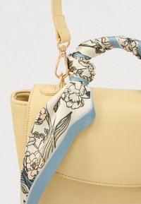 Sac à main en cuir jaune clair avec une fermeture dorée et un foulard floral torsadé aux tons bleus et crème enroulé autour de la poignée.