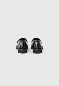 Black leather loafers with a smooth finish, round toe, and low rubber sole. Features a back strap and subtle stitching detail.