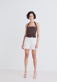 Brown halter top with ruched design, paired with white, drawstring shorts. Model stands on a light background, featuring strappy sandals.