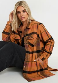 Brun och orange rutig skjorta med svarta accenter, två bröstfickor, knappstängning och långa ärmar, tillverkad av ett mjukt tyg.