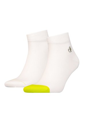 Weiße Knöchelsocken mit strukturiertem Strick, ausgestattet mit einer leuchtend gelben Zehenkappe und einem kleinen grünen Logo in der Nähe des Bündchens.