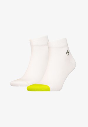 White ankle socks with a textured knit, featuring a bright yellow toe cap and a small green logo near the cuff.