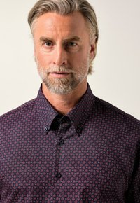 Camicia blu navy con motivo geometrico in bordeaux e bianco, dotata di colletto strutturato e chiusura con bottoni. Tessuto dalla superficie liscia.