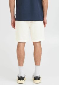White textured shorts with cuffed hems, shown from the back, paired with black and cream sneakers and white crew socks.