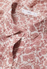 Bluse mit floralem Muster in Rot- und Beigetönen, ausgestattet mit einem Punktkragen und Knopfverschluss. Hergestellt aus leichtem Stoff mit weicher Textur.