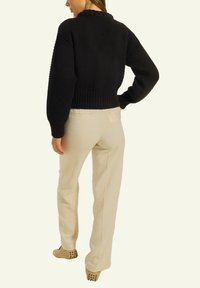 Schwarzer Strickpullover mit strukturiertem Muster und geripptem Saum, kombiniert mit hellbeigen Hosen und beigen Schuhen mit Gummipunkt-Akzenten.