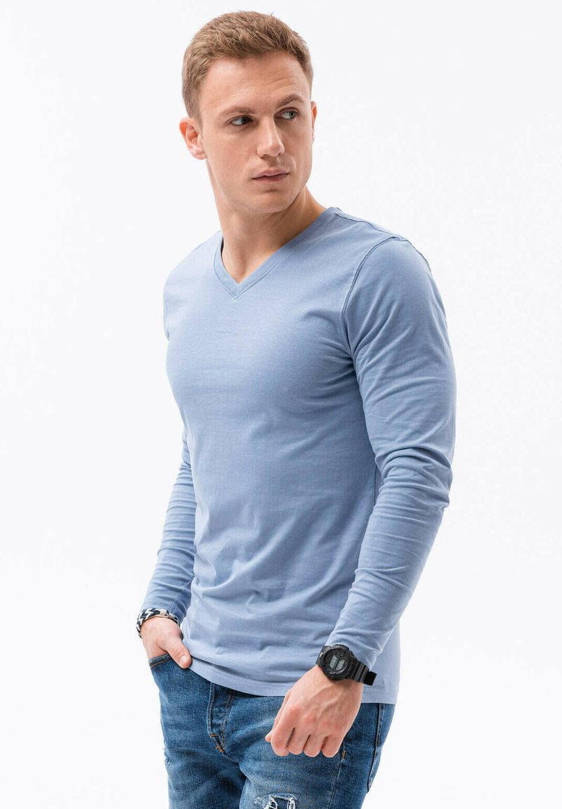 Světle modrá dlouhá halenka s výstřihem do V, která se vyznačuje jemnou texturou a přiléhavým střihem, v kombinaci s roztrhanými modrými džíny.