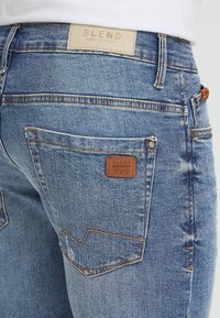 Light blue denim jeans with a leather label on the waistband. Features double-stitched seams and a classic pocket design.