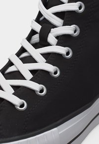 Juoda aukšta sportbačių su baltais raišteliais, praveržtais per metalines akutės, ir baltu guminiu padu su juoda juostele.