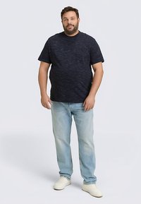 Dunkel marineblaues T-Shirt mit kurzen Ärmeln und strukturiertem Muster, kombiniert mit hellblauen Jeans mit geradem Schnitt und weißen Sneakers. Lässige Passform, keine sichtbaren Logos.