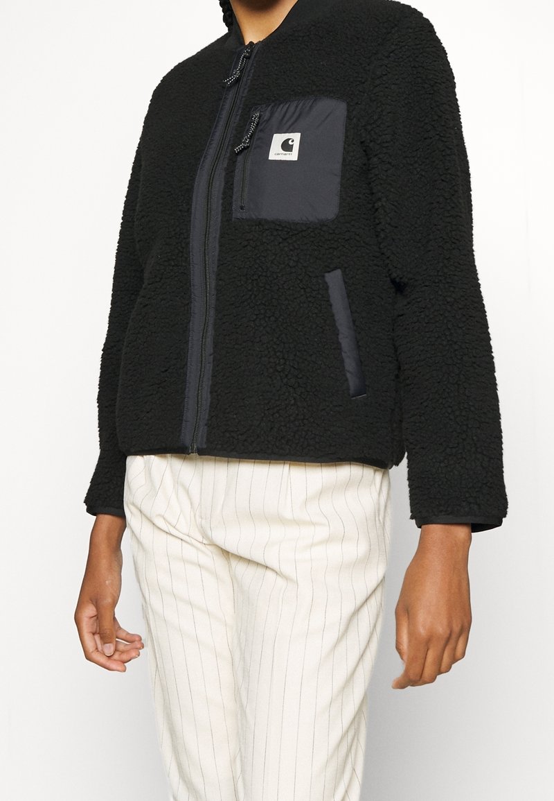 Czarna polarowa kurtka na zamek z kontrastową kieszenią z czarnego materiału i akcentami z tkaniny, z teksturowaną powierzchnią i luźnym fasonem.