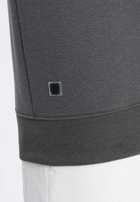 Felpa grigia con tessuto testurizzato, polsini a coste e un piccolo badge del logo vicino all'orlo. Cuciture a contrasto lungo il bordo inferiore.