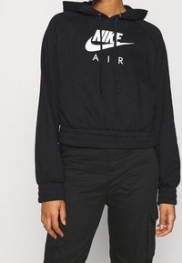 Black cropped hoodie made of soft fabric, featuring a drawstring hood and elastic waistband. Displays white Nike Air logo on the front.