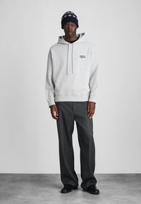 Gray hoodie with drawstrings and front logo, paired with dark gray pleated pants and black shoes. Featured knit hat with navy coloring.