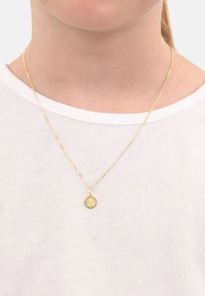 Collana d'oro con un piccolo pendente rotondo che presenta un design di fiore inciso, indossata su una maglietta bianca a girocollo.