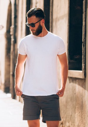 White cotton t-shirt with short sleeves, paired with gray shorts. The fabric is smooth, offering a relaxed fit and simple design.