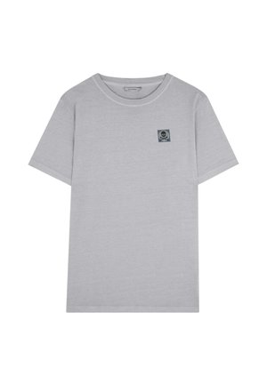 Helles graues T-Shirt mit kurzen Ärmeln und Rundhalsausschnitt, mit einem kleinen dunklen Patch mit Totenkopf und gekreuzten Knochen auf der linken Brust.