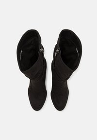 Bottes mi-mollet en daim noir avec fermetures éclair sur le côté intérieur, vues de dessus sur fond blanc.