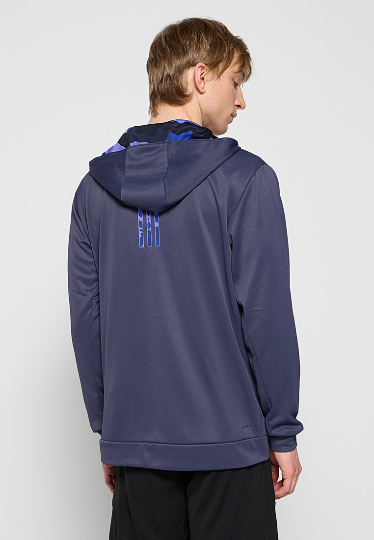 Haut à capuche d'athlétisme marine avec une texture lisse, présentant une doublure de capuche à motifs bleus et trois accents verticaux au dos.