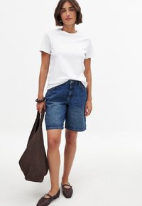 Camiseta de algodón blanca, pantalones cortos de mezclilla azules, bolso de hombro de cuero marrón, zapatos planos trenzados marrones. Diseño sencillo, corte relajado y estilo casual.