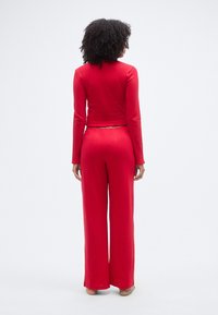 Ensemble assorti rouge composé d'un haut côtelé à manches longues et d'un pantalon à jambes larges. Le haut présente une coupe courte et un ourlet festonné.