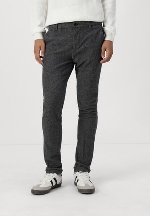 Pantalons slim gris texturé avec une taille standard et des poches avant, associés à des baskets blanches et grises.