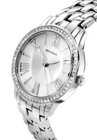 Montre bracelet en argent avec un cadran rond, des chiffres romains et des embellissements en cristal sur la lunette. Bracelet en métal à maillons avec une finition brillante.