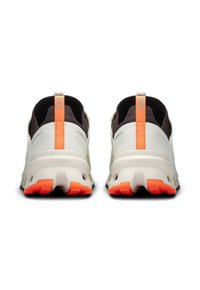 Baskets avec une tige synthétique blanche et grise, semelle en caoutchouc noir et accents orange vif. Comprend un talon texturé et un détail de logo.