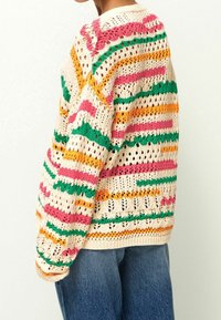 Pull tricoté multicolore avec rayures roses, orange, vertes et crème, et motifs en point ajouré. Manches longues et ourlet côtelé.