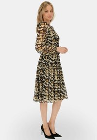 Sukienka z długim rękawem, do kolan, wykonana z przezroczystej tkaniny z czarno-beżowo-brązowym wzorem w zygzak; plisowany dół i okrągły dekolt.