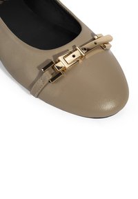 Beige Lederflats mit spitzem Zehenbereich und einem auffälligen goldfarbenen Hardware-Akzent über dem Vorderfuß, mit einer strukturierten Oberfläche.