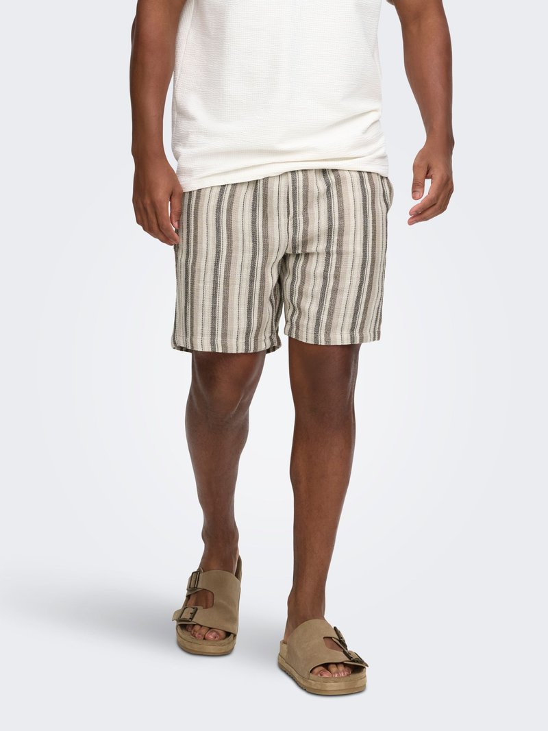 Homme portant un short beige et marron à rayures verticales, une chemise blanche texturée à manches courtes et des sandales réglables couleur sable avec boucle.