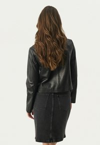 Schwarze Lederjacke mit einem cropped Design, kombiniert mit einem dunklen Denim-Bleistiftrock, der über Gesäßtaschen und eine subtile Nahtdetails verfügt.