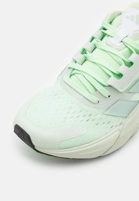 Scarpa sportiva verde chiaro con tomaia in rete traspirante, dettagli testurizzati e suola in gomma nera. Presenta lacci e sovrapposizioni sintetiche.