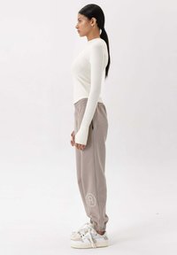 Witte geribde langemouwen top gecombineerd met lichtgrijze sweatpants met een elastische tailleband en logo. Schoeisel bestaat uit witte sneakers.