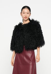 Veste courte en fausse fourrure noire à la surface texturée et duveteuse avec des manches larges, portée avec une jupe en cuir bordeaux.