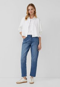 Biely l nenový skrátený top, voľný strih, gombíkový predný diel; skombinovaný s svetlo modrými rovnými džínsami a béžovými teniskami s bielymi akcentmi.