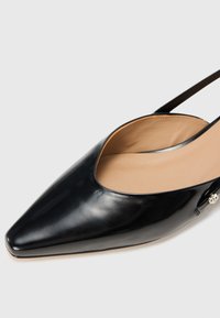 Black leather slingback pump with a pointed toe, open design, and a smooth texture. Features a subtle metallic accent on the side.