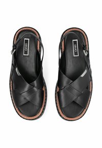 Zwarte leren sandalen met een kruisbandontwerp, een verstelbare enkelriem en een bruine accenten op de zool met een gestructureerde afwerking.