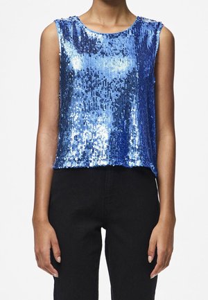 Vrouw draagt een mouwloze, felblauwe top met pailletten, gecombineerd met een hoge taille zwarte broek, tegen een effen witte achtergrond.