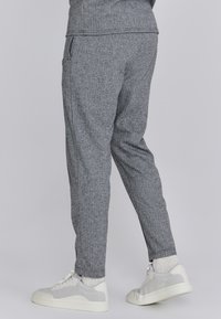 Szürke houndstooth mintás nadrág, keskeny fazonú, oldalsó zsebekkel, fehér hálós sportcipőkkel és kötött zoknikkal párosítva.