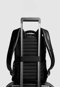 Zwarte rugzak met gewatteerde panelen, verstelbare bandjes en een achterste trolleyband. Voorzien van een stevige handgreep en een gladde textuur.