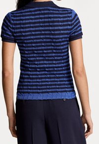 Texturerad stickad polo t-shirt med blå och marinblå horisontella ränder, korta ärmar och ribbad nederkant. Bakifrån visas ett detaljerat mönster.