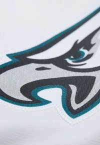 Der weiße Stoff weist ein auffälliges schwarzes und türkisfarbenes Logo der Philadelphia Eagles auf, das mit kunstvollen Stichen und strukturierten Oberflächendetails versehen ist.
