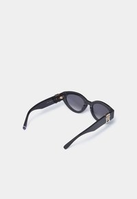 Sorte cat-eye solbriller med mørke linser, som har gull hardware-detaljer og stripet dekor på endene av brillestengene. Glanset finish.